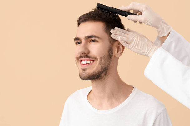 Docteur brossant les cheveux du jeune homme sur fond beige, gros plan - Photo, image