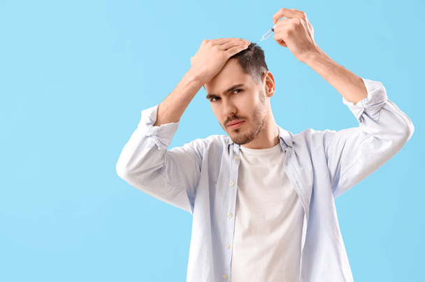 Young brunette man giving himself injection for hair growth on blue background - Photo, Image