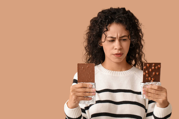 Ajattelevainen nuori afroamerikkalainen nainen, jolla on makea suklaapatukka ruskealla taustalla - Valokuva, kuva