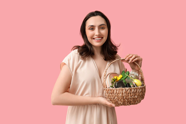 Glückliche junge Frau hält Osterkorb mit dekorativer Kosmetik auf rosa Hintergrund - Foto, Bild