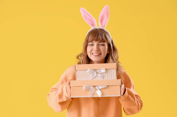 Giovane ragazza con orecchie di coniglio di Pasqua e regali su sfondo giallo - Foto, immagini