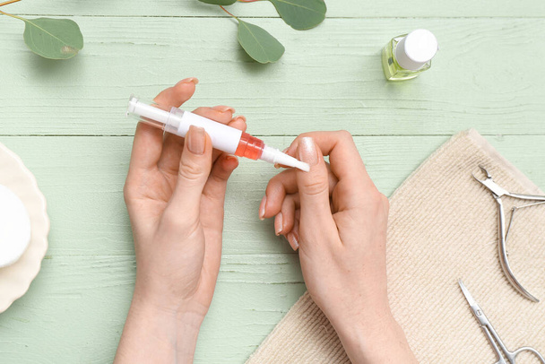 Female hands applying cuticle oil onto fingernails, eucalyptus twig and towel on green wooden background - Photo, Image