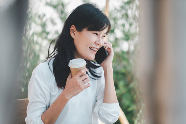 Iloinen nainen, jolla on miellyttävä keskustelu matkapuhelimellaan nauttien kupin kahvia ulkona. - Valokuva, kuva