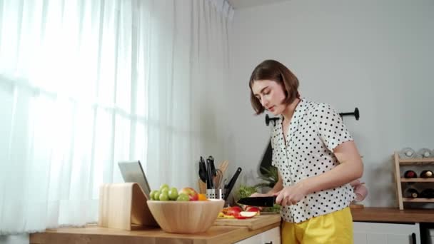 Kaukasische moeder bereiden voedsel voor het maken van salade, terwijl op zoek naar voedsel recept in laptop in de moderne keuken. Actief ervaren huishoudster werken en koken ontbijt met behulp van verse groenten. Pedagogie. - Video