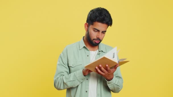 Gelukkig ontspannen glimlachende Indiase jongeman lezen grappig interessant sprookje verhaal boek, vrijetijdsbesteding, kennis wijsheid, onderwijs, leren, studeren, wow. Arabian Hindoe kerel geïsoleerd op gele achtergrond - Video