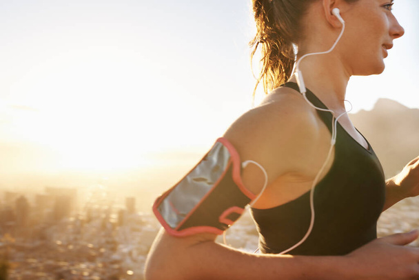Woman, running and listening to music with earphones for workout, training or outdoor exercise. Young female person or runner with smile and headphones for audio streaming or cardio on mockup space. - Photo, Image