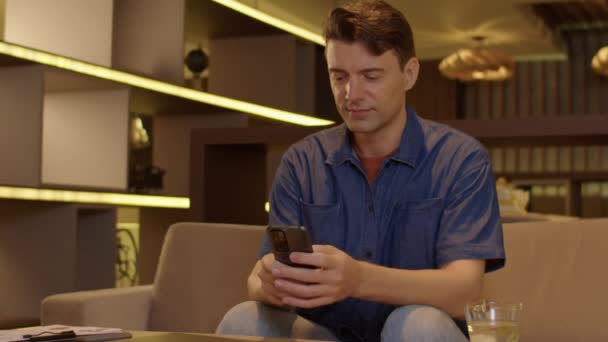 Medium lang portret van vrolijke blanke zakenman werken op de smartphone en kijken naar de camera - Video