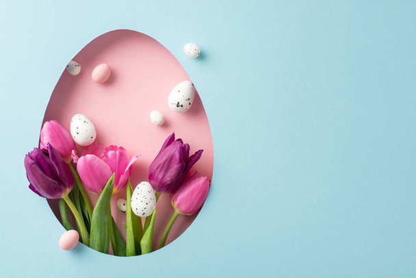 Delightful Easter inspiration concept: overhead shot showcasing vibrant tulips and multicolored quail eggs emerging from an egg-shaped cutout on a soft blue backdrop, leaving space for your message - Photo, Image