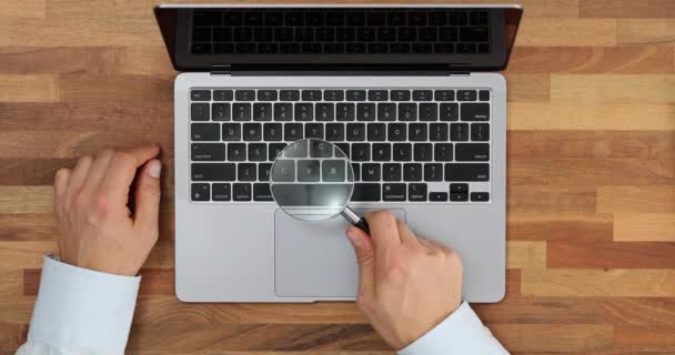 Zbliżenie człowieka ze szkłem powiększającym przez klawiaturę laptopa. Hakowanie haseł i kradzież tożsamości - Materiał filmowy, wideo