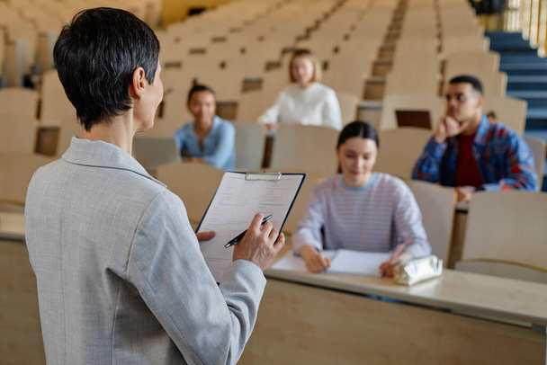 Zadní pohled učitele čtení zprávu pro studenty, zatímco sedí za stolem během přednášky na univerzitě - Fotografie, Obrázek