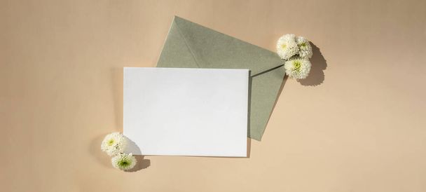 Hermosas flores blancas en sobre verde postal sobre fondo beige, espacio de copia de papel vacío para texto, primavera, tarjeta de felicitación para vacaciones. Concepto de entrega - Foto, Imagen