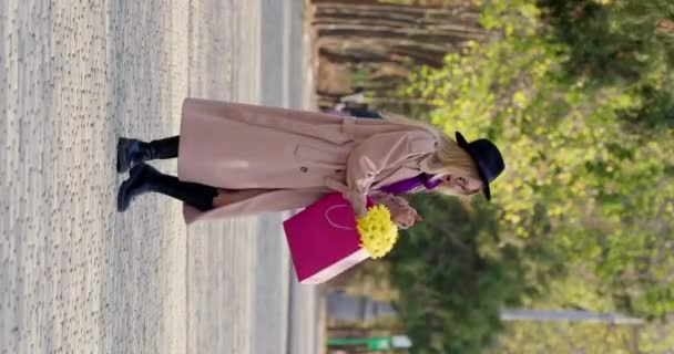 Elegancka kobieta wyciąga ładny bukiet świeżych kwiatów z jaskrawo kolorowej torby i uśmiecha się jak pachnie rośliny. Mieszkaniec miasta pławiący się w słońcu - Materiał filmowy, wideo