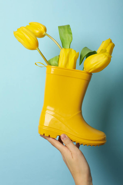 Żółty gumowy but z kwiatami w dłoni na niebieskim tle - Zdjęcie, obraz