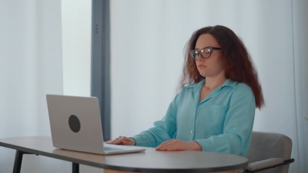 Une femme est assise à une table, absorbée dans son travail sur un ordinateur portable. - Séquence, vidéo