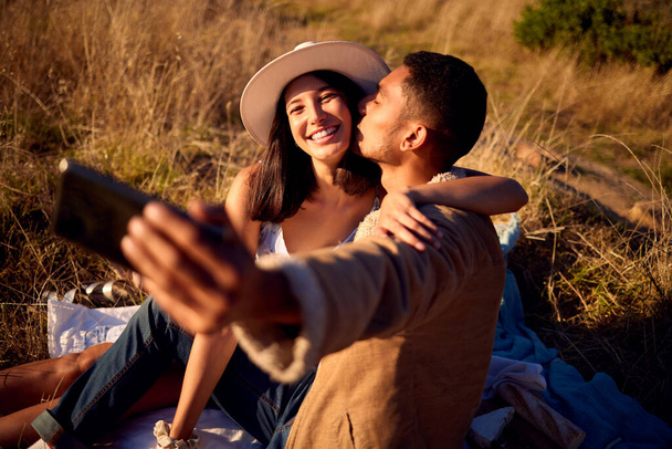 Pár polibek v selfie s objetím, venkovní a piknik v přírodě, láska s chytrým telefonem, technologie a šťastný spolu. Telefon pro fotografii, muž a žena úsměv na obrázku s cestovní a letní datum. - Fotografie, Obrázek