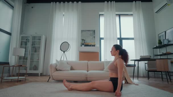 Er zit een vrouw op de vloer in een typische woonkamer. Ze is rustig zitten, ontspanning stretching oefeningen yoga praktijk. - Video