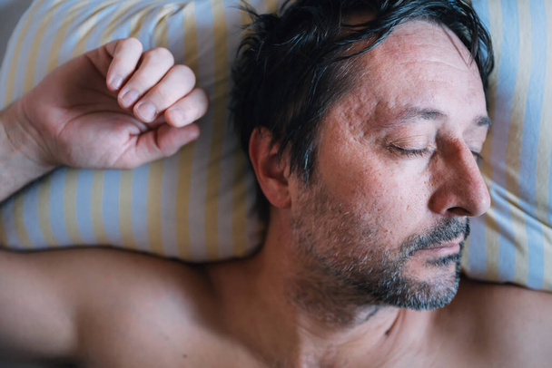Ο άνθρωπος κοιμάται στο κρεβάτι σε ένα μαξιλάρι το πρωί, ακριβώς από πάνω - Φωτογραφία, εικόνα