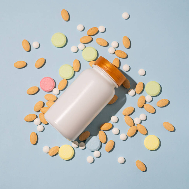 Assorted pills and nutritional supplements in different colors with white bottle on a light blue background. Health medicine concept. Top view and copy space.  - Photo, Image