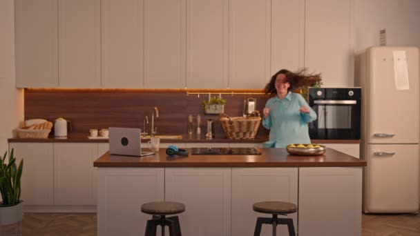 Μια γυναίκα γιορτάζει την επιτυχία ενθουσιασμένοι χορό σε μια κουζίνα, ευτυχισμένη και χαρούμενη στο σπίτι  - Πλάνα, βίντεο