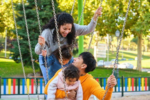 Λατινική οικογένεια με δύο παιδιά που παίζουν μαζί σε μια παιδική χαρά. Ισπανική οικογένεια. - Φωτογραφία, εικόνα