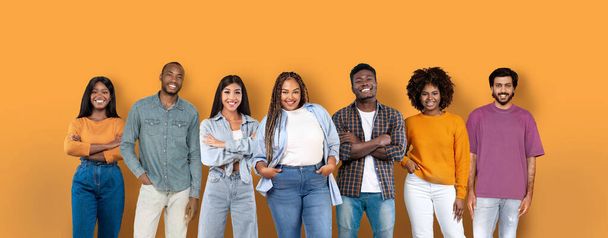 Seven diverse and stylish young adults with confident smiles, standing casually in a line against a warm orange background, embodying togetherness and modernity, studio, panorama - Foto, immagini