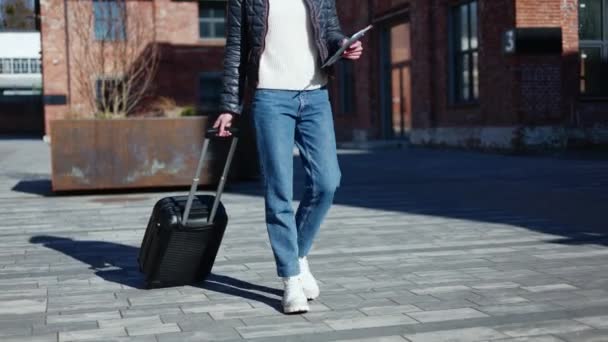 Oříznutý pohled neznámé ženy kráčející s cestovním kufrem a držící smartphone s balíčkem dokumentů. Uvolněná žena v džínách a svetru a jít strávit víkend v all inclusive resort. - Záběry, video