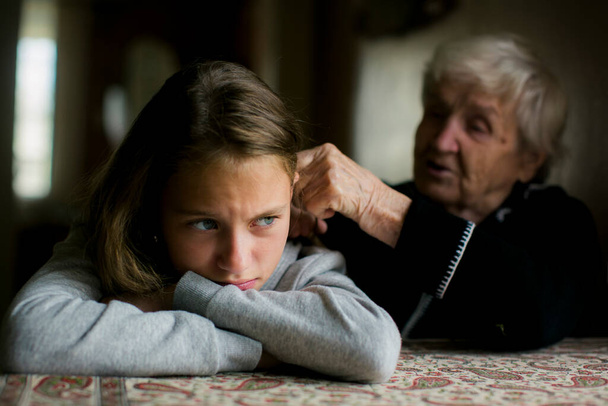 Una abuela cepilla el pelo de su descontenta nieta.   - Foto, imagen