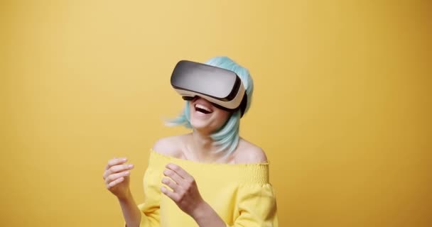 Статичний знімок веселої молодої жінки в гарнітурі VR з блакитним волоссям посміхається і жестикулює великим пальцем вгору, а потім відвертається, досліджуючи кіберпростір на жовтому тлі. жіноча схвалення віртуальної реальності
 - Кадри, відео
