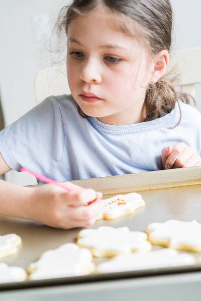 Una scena commovente di una bambina che scrive con attenzione Mi dispiace sui biscotti allo zucchero con coloranti alimentari, i biscotti splendidamente inondati di glassa reale bianca. - Foto, immagini
