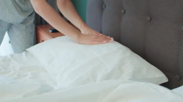 In een serene slaapkameromgeving, een jonge vrouw handen zorgvuldig aan te passen een kussen, doordrenkt van de ochtend met een gevoel van rust en routine - Video