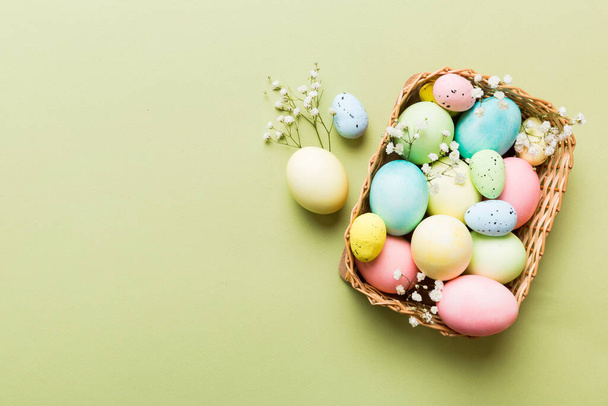 Boldog húsvéti kompozíciót. Húsvéti tojás kosárban, színes asztalon cigányvirággal. Természetes festett színes tojás háttér felülnézet másolási hely. - Fotó, kép