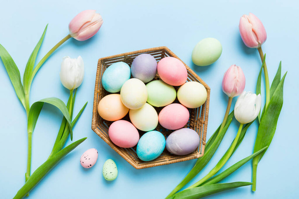 Feliz composición de Pascua. Huevos de Pascua en canasta sobre mesa de colores con Tulipanes amarillos. Huevos coloridos teñidos naturales vista superior de fondo con espacio de copia. - Foto, imagen