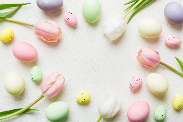 Feliz composición de Pascua. Huevos de Pascua en mesa de colores con tulipanes amarillos. Huevos coloridos teñidos naturales vista superior de fondo con espacio de copia. - Foto, imagen