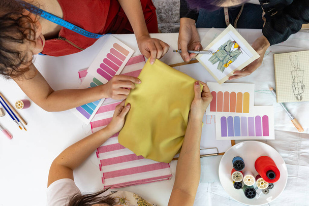 Team of fashionable freelance dressmaker and customer choosing design and fabric color for new custom dress while working in artistic workshop studio for fashion design and clothing business industry - Photo, Image
