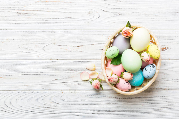 Boldog Húsvétot! Húsvéti tojás kosárban a színes asztalra sárga rózsákkal. Természetes festett színes tojás háttér felülnézet másolási hely. - Fotó, kép