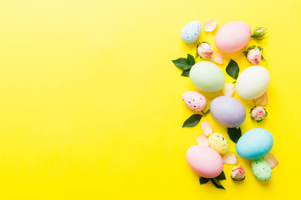 Veselé Velikonoce. Velikonoční vajíčka na barevném stole se žlutými růžemi. Přírodní barvené barevné vejce pozadí horní pohled s kopírovacím prostorem. - Fotografie, Obrázek