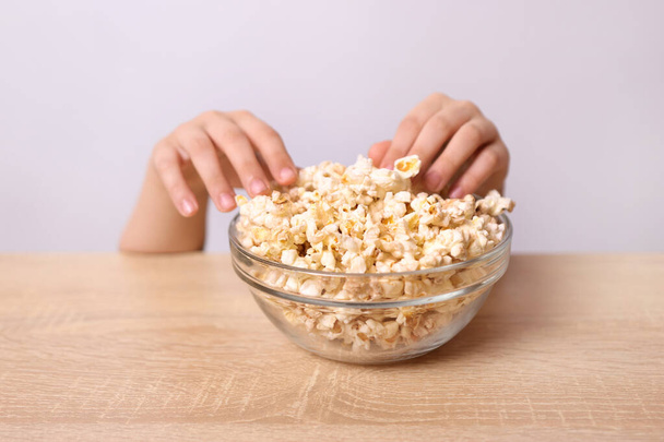 Le mani dei bambini sono visibili da sotto il tavolo, cercando di prendere i popcorn dal tavolo.. - Foto, immagini