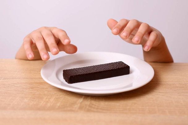 Egy gyerek kezei láthatók az asztal alól, amint egy csokis ostyát próbál leszedni az asztalról.. - Fotó, kép