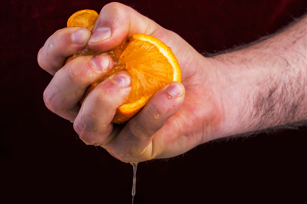 männliche Hand quetscht Orange auf Maulbeergrund. - Foto, Bild