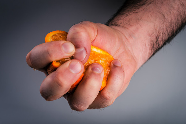 Male hand squeezing orange on mulberry background. - Photo, Image