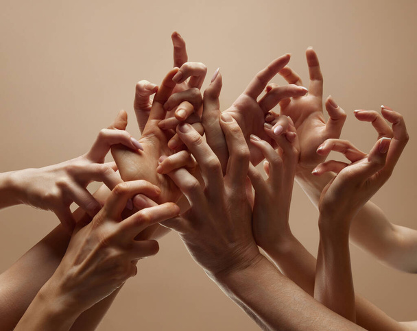 Множественные переплетенные руки под разными углами создают единство на бежевом студийном фоне, символизирующем человеческую связь, гармонию. Концепция человеческого прикосновения, красоты и ухода, спа-процедуры. - Фото, изображение