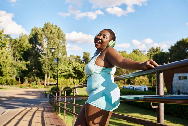 Une Afro-Américaine aux cheveux bouclés, vêtue d'une robe bleue et blanche, se penche élégamment sur un rail tout en profitant de la musique. - Photo, image