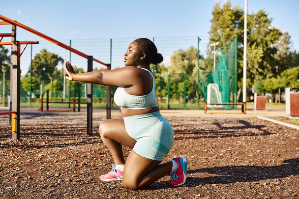 Una donna afroamericana in abbigliamento sportivo accovacciata davanti a un parco giochi, che incarna positività e forza del corpo. - Foto, immagini