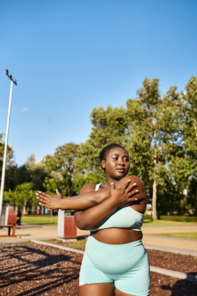 Eine selbstbewusste Afroamerikanerin mit kurvigem Körperbau wird in einem blauen Sport-BH-Top und kurzen Hosen bei Outdoor-Übungen gesehen.. - Foto, Bild