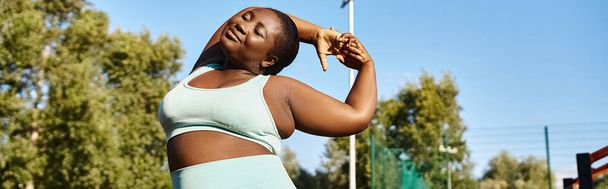 Uma mulher afro-americana em sportswear confiantemente esticando os braços ao ar livre, abraçando sua positividade corporal. - Foto, Imagem