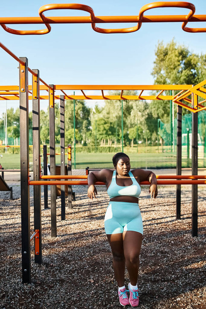 Eine Afroamerikanerin in blauer Sportbekleidung steht selbstbewusst auf einem Spielplatz und verkörpert Körperpositivität und Freiheit. - Foto, Bild