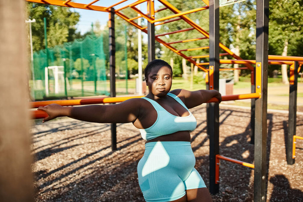 Una donna afroamericana in abbigliamento sportivo colpisce una posa di fronte a un parco giochi, mostrando positività del corpo. - Foto, immagini