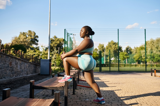スポーツウェアのアフリカ系アメリカ人女性は,屋外の木製のベンチの上に優雅に取り組んでいると考えています.. - 写真・画像
