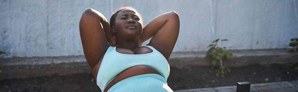 Una mujer afroamericana confiada en ropa deportiva ejecuta hábilmente un soporte de mano al aire libre, personificando la positividad corporal. - Foto, imagen