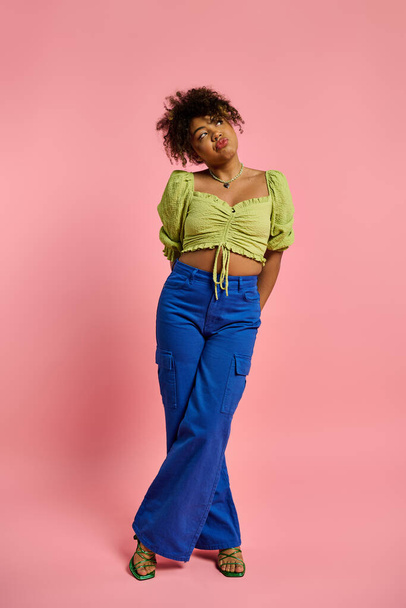 Elegante donna afroamericana in top giallo e pantaloni blu in posa su uno sfondo vibrante. - Foto, immagini